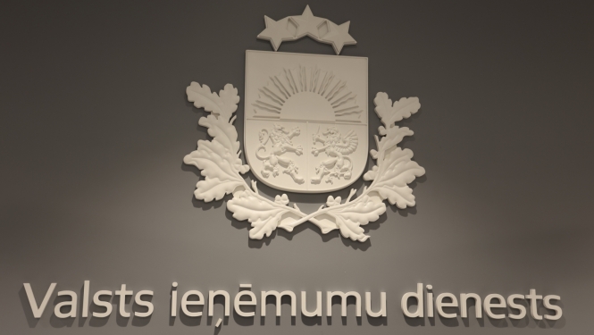 Balts ģērbonis un uzraksts Valsts ieņēmumu dienests uz pelēkas sienas